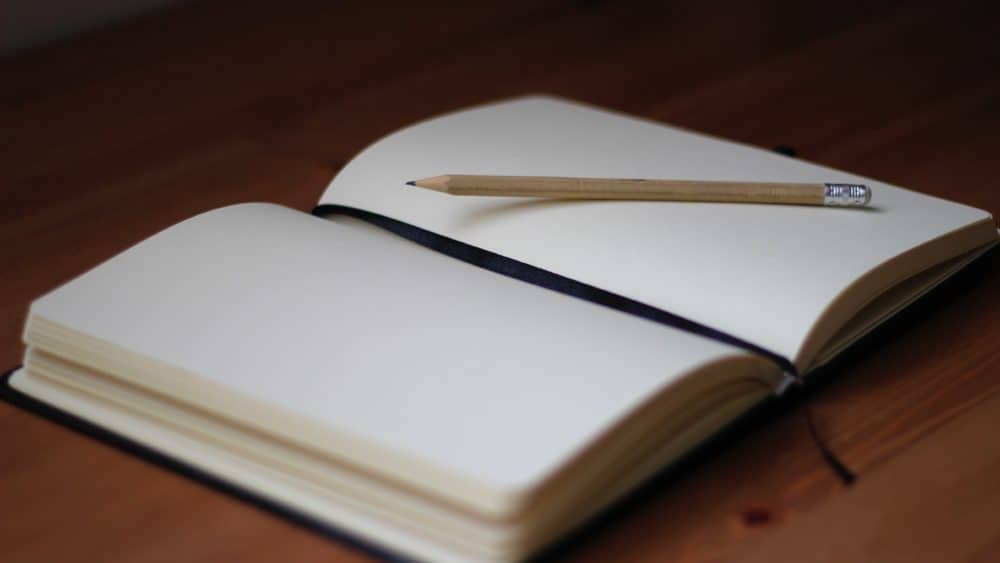 An open journal placed on a table, empty despite the pencil resting on its pages.