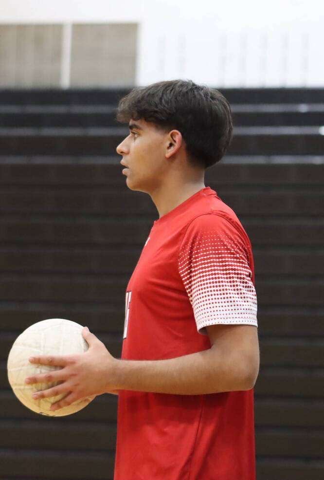 Male student athlete in red jersey holds volleyball